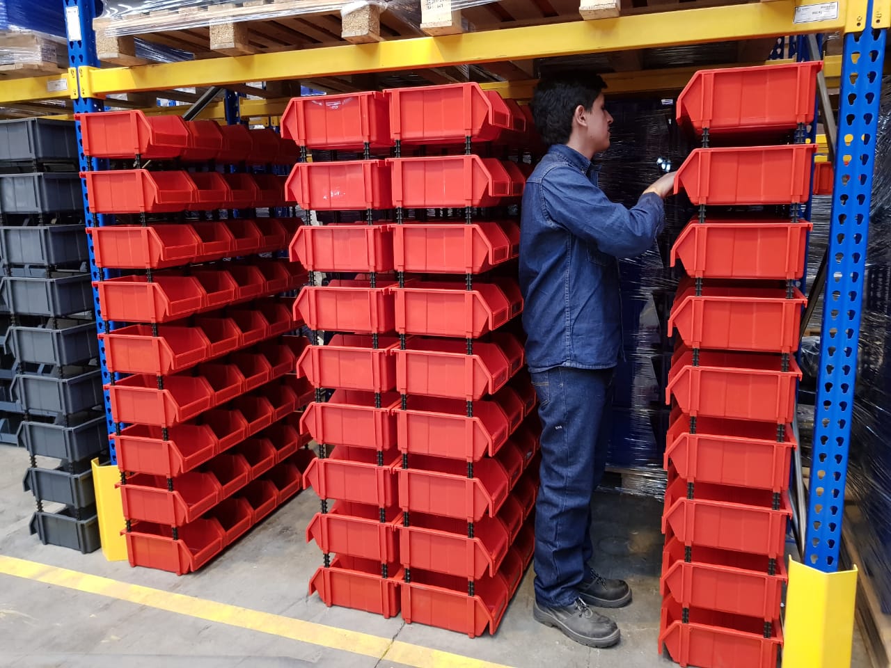 Un hombre está parado frente a una fila de contenedores rojos en un almacén.