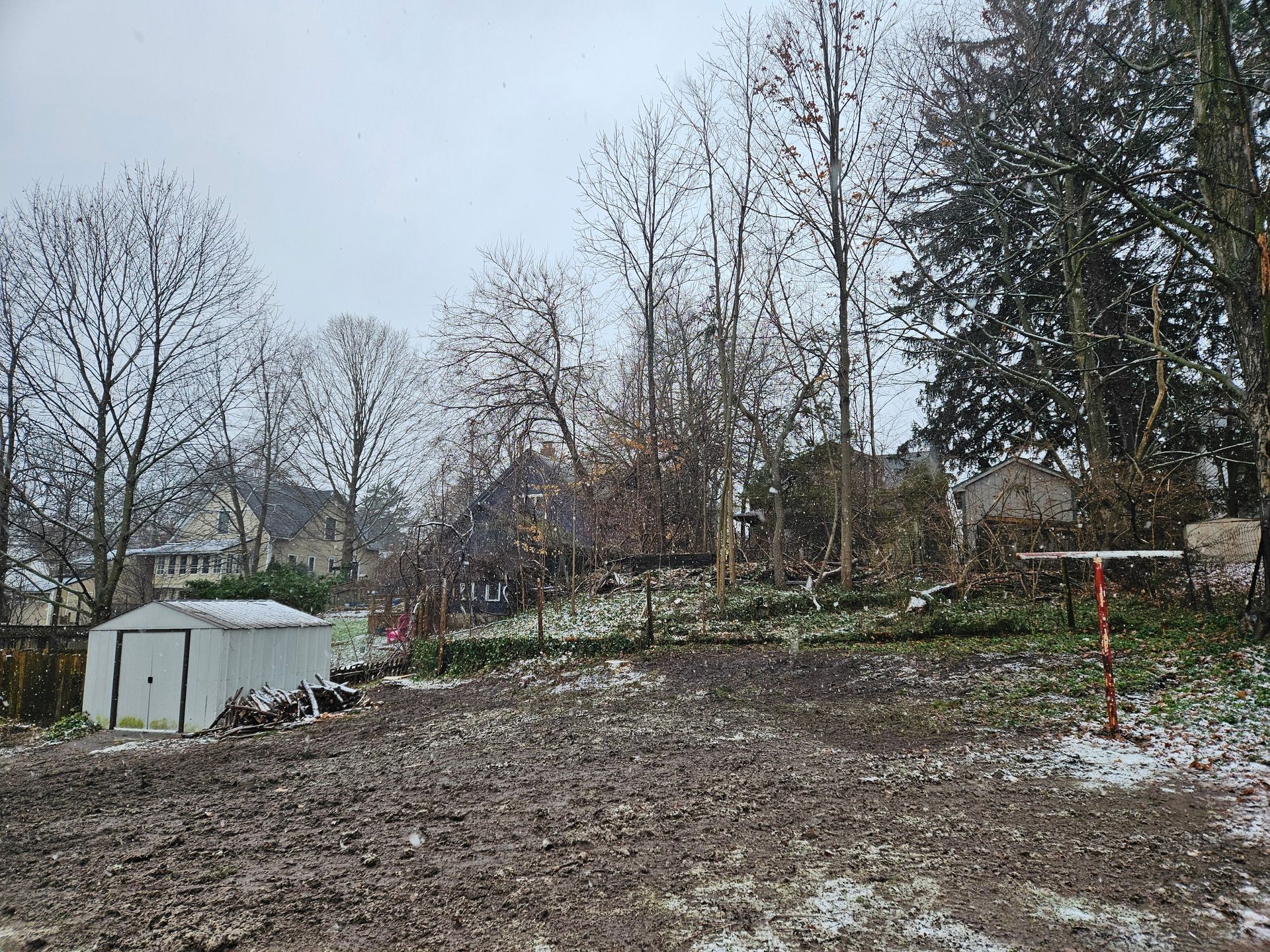 A muddy yard with a white shed and trees in the background.
