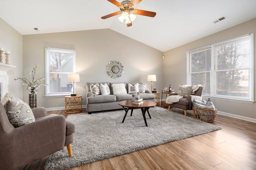 Bright living room with gray sofa, chairs, coffee table, shag rug, and large windows under vaulted ceiling