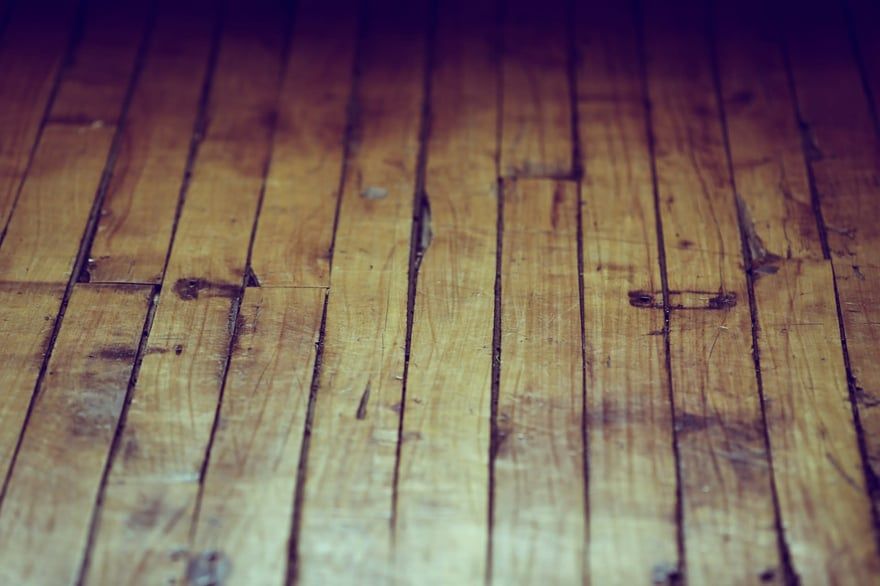 Purple-tinted wooden floorboards with visible grain and scratches