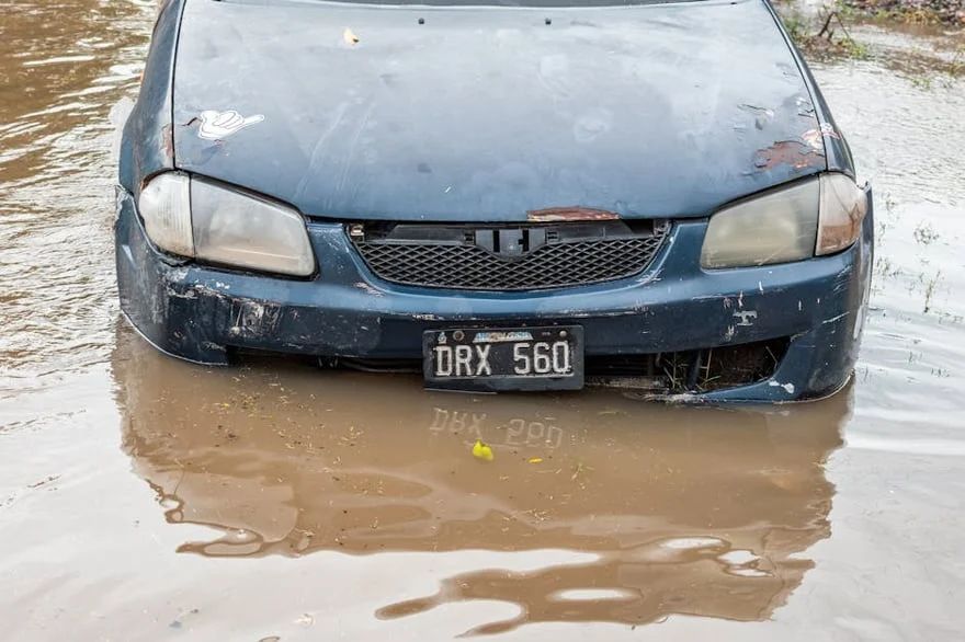 Blue car partially submerged in muddy floodwater, front view