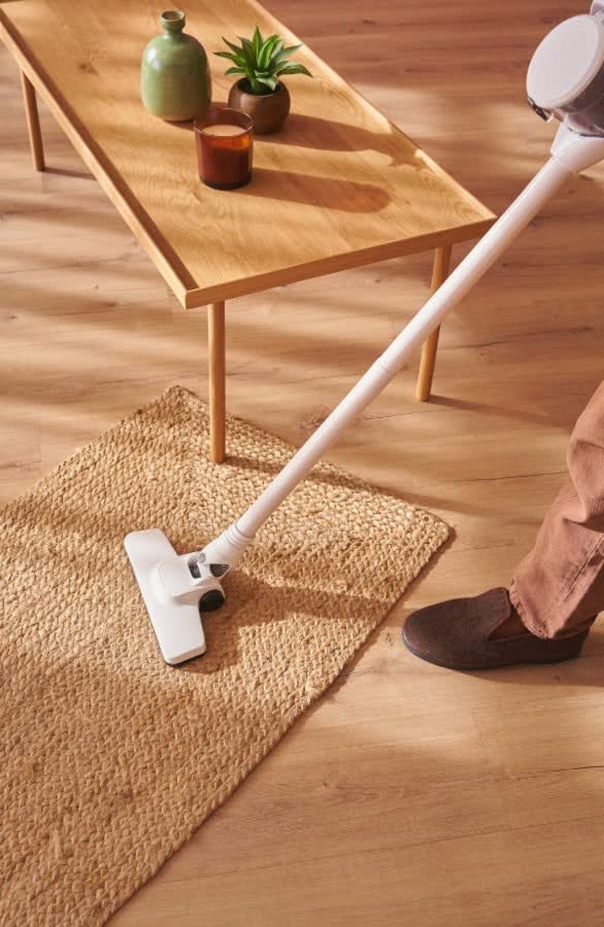Person vacuuming a beige rug in a bright living room beside a wooden coffee table