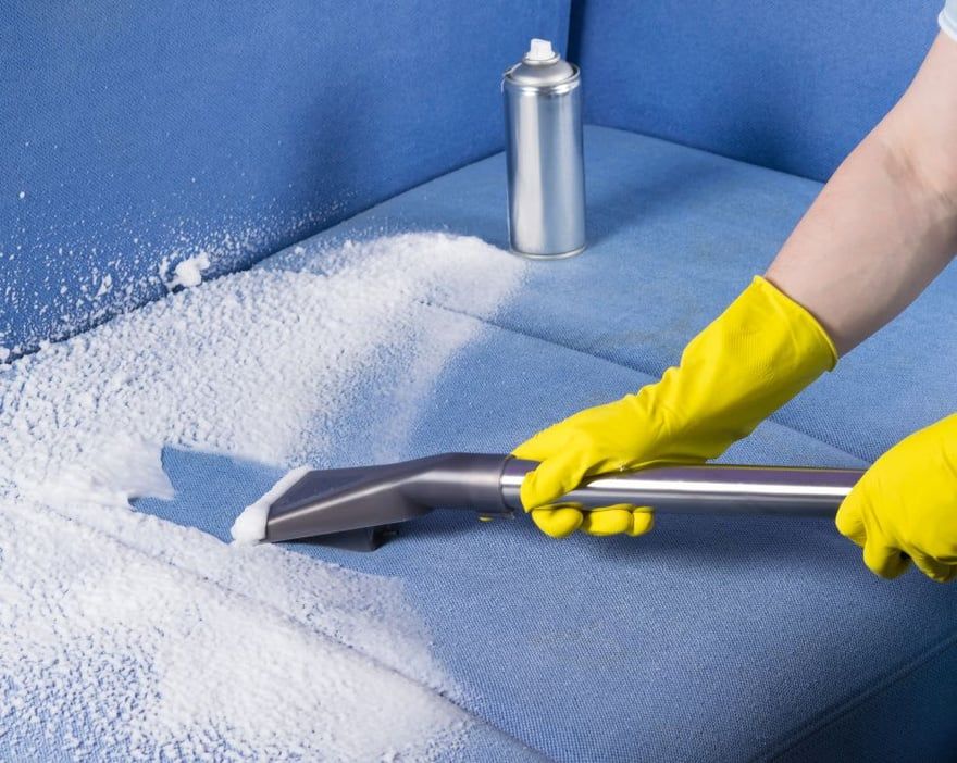 Yellow-gloved hands vacuuming white powder from a blue couch with a handheld tool