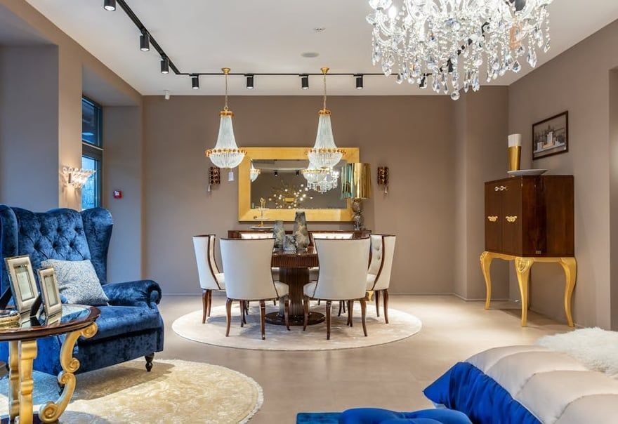 Elegant living and dining room with blue sofa, round table, chandelier, and mirrored wall decor