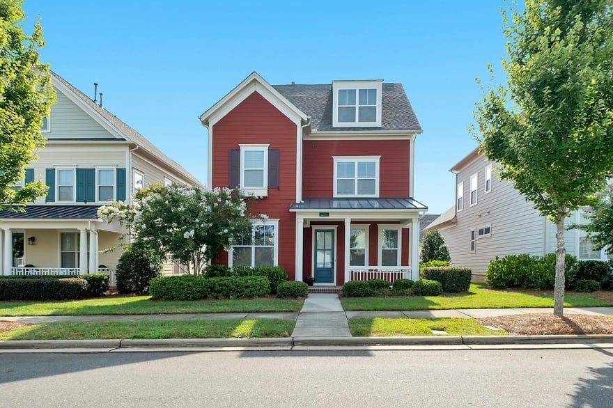 Red two-story house with white trim and a front porch on a tree-lined suburban street