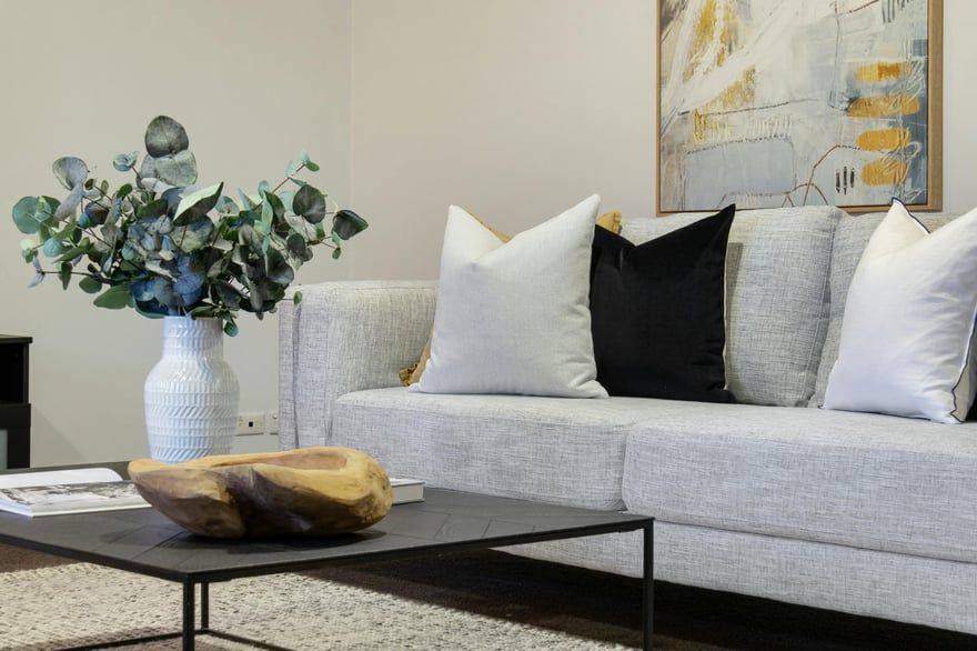 Modern living room with gray sofa, white pillows, black coffee table, and a vase of greenery