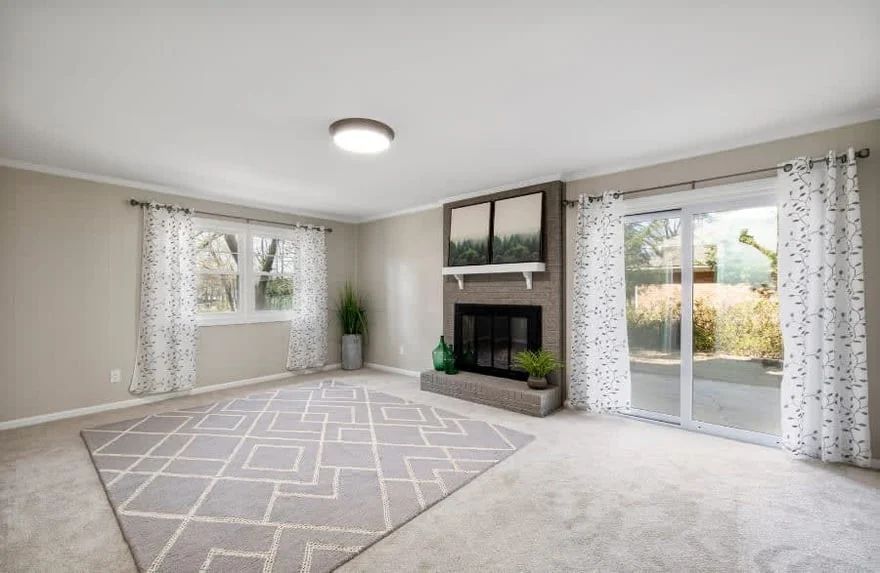 Bright living room with gray rug, fireplace, large windows, and sliding glass doors opening outside