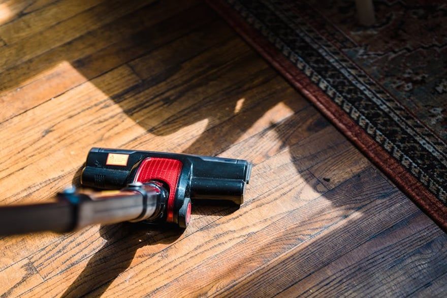 Vacuum cleaner on wooden floor in warm sunlight, near a patterned rug