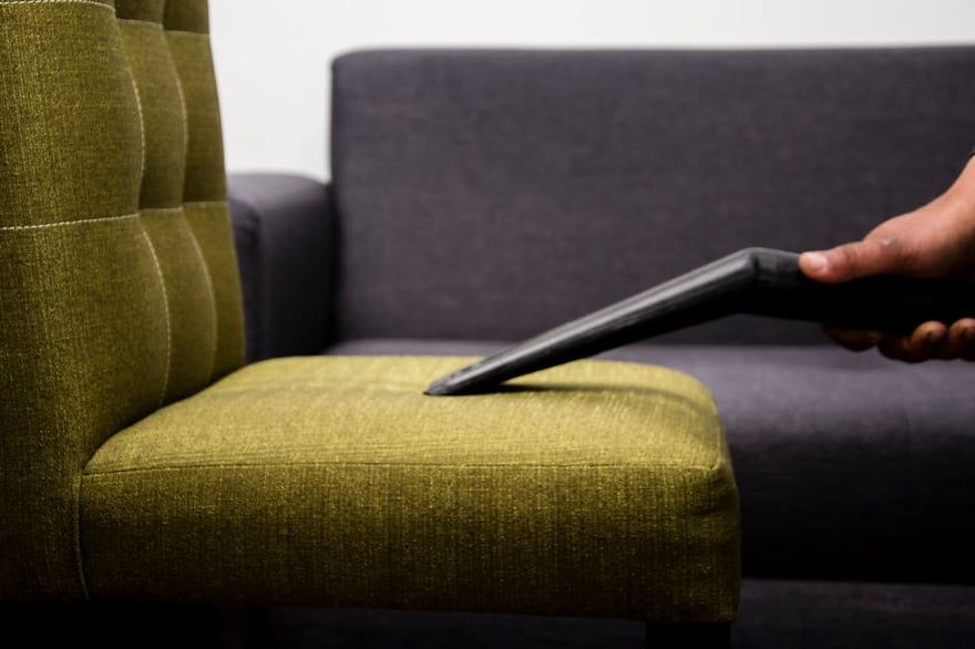 Hand using a laptop on a green chair beside a gray sofa