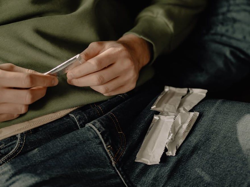 Person rolling a small white paper on a lap beside several chewing gum pack.