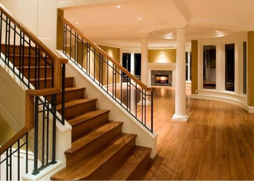 Warm-lit modern foyer with wood floors, staircase, columns, and a fireplace.