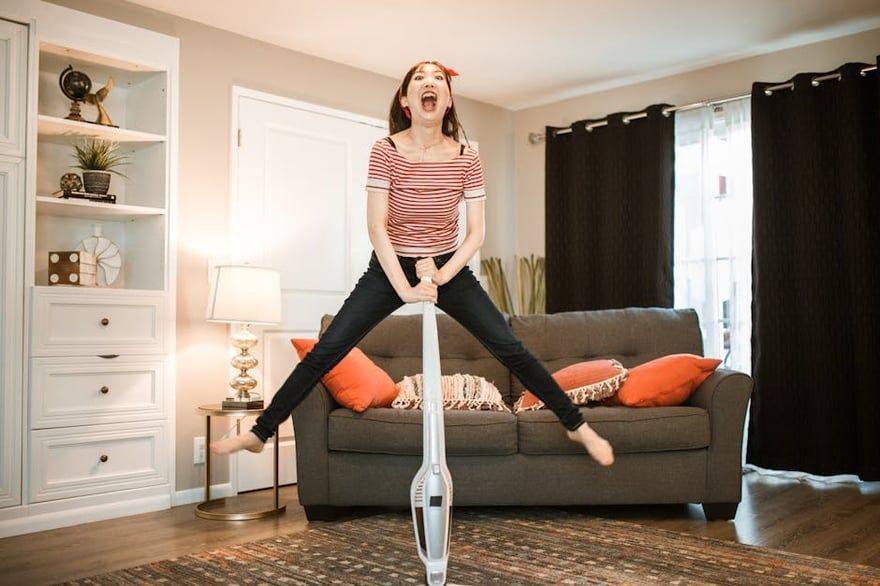 Person balancing on a pogo stick in a living room, wearing a striped shirt and black pants.