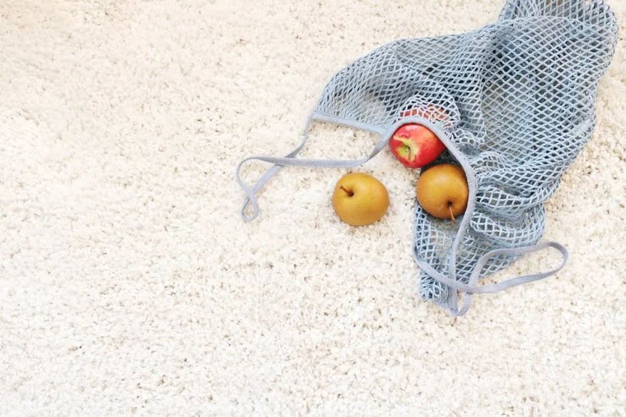 Apples in a blue mesh produce bag on a light speckled surface