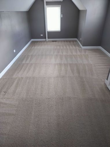 Empty gray-carpeted room with sloped ceilings and a window at the far end