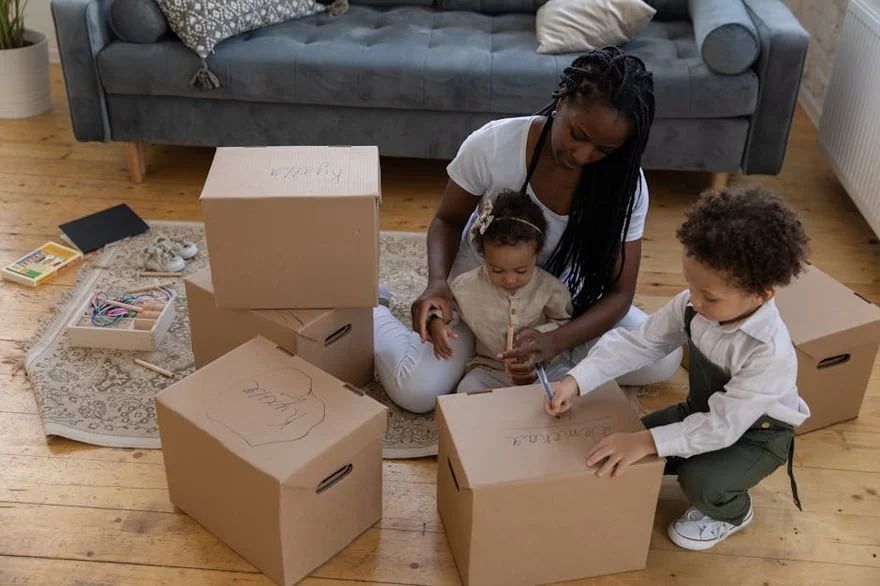 Family unpacking cardboard boxes on a wooden floor in a living room with a gray couch