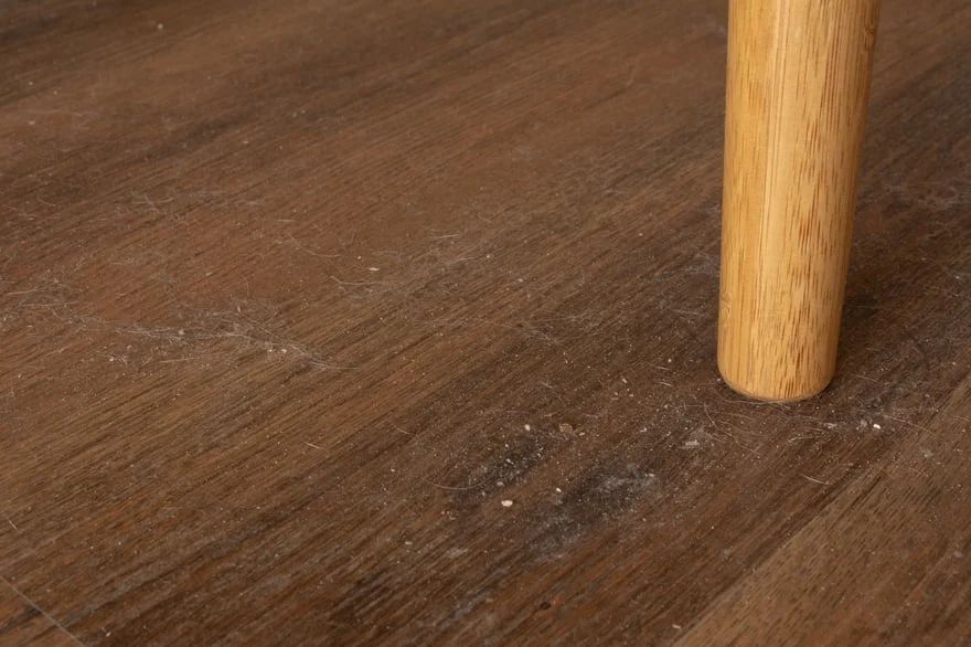 Wooden table leg on a dark brown wooden floor with visible dust and wear