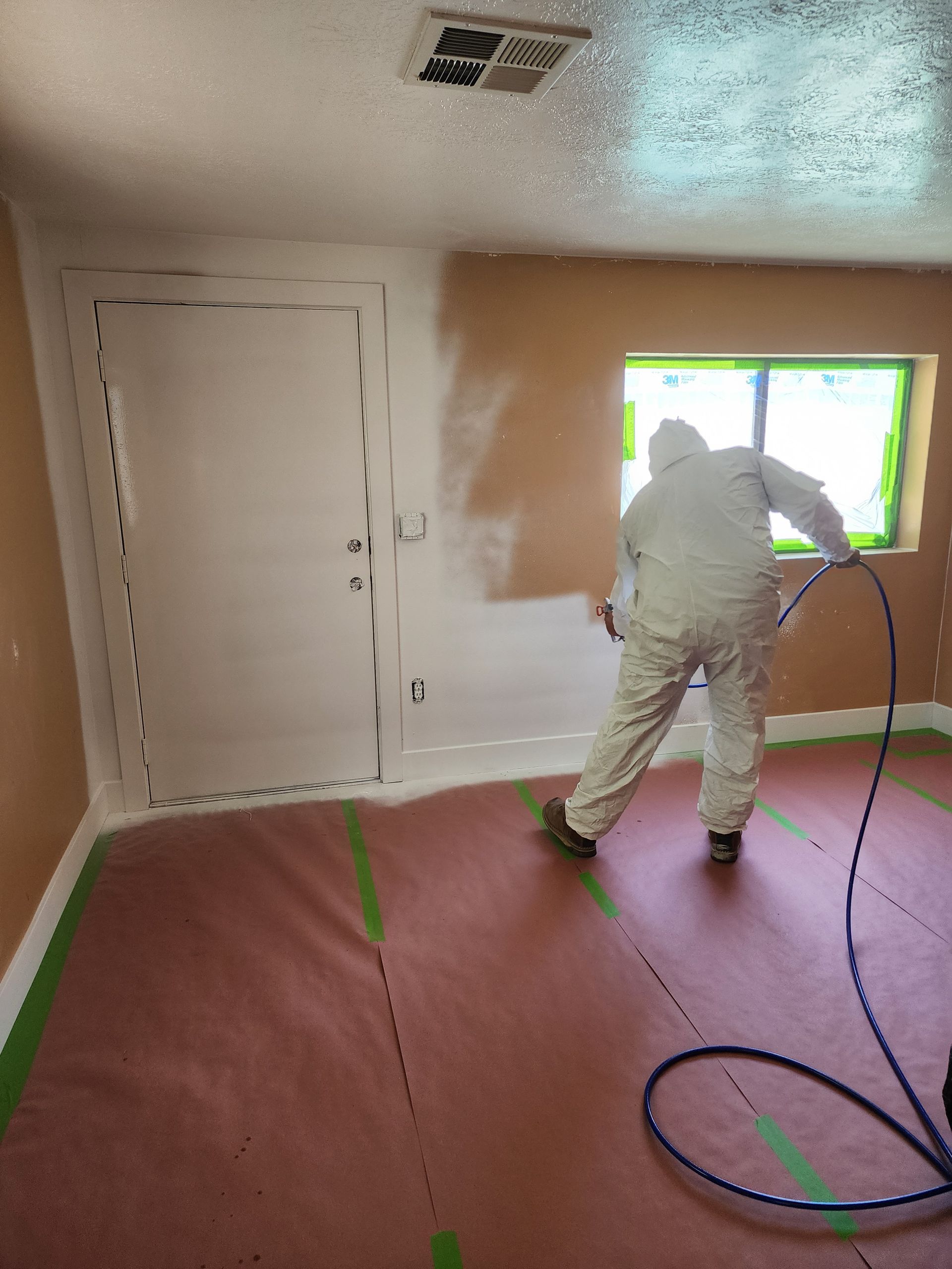 A man is painting a wall in a room with a sprayer.
