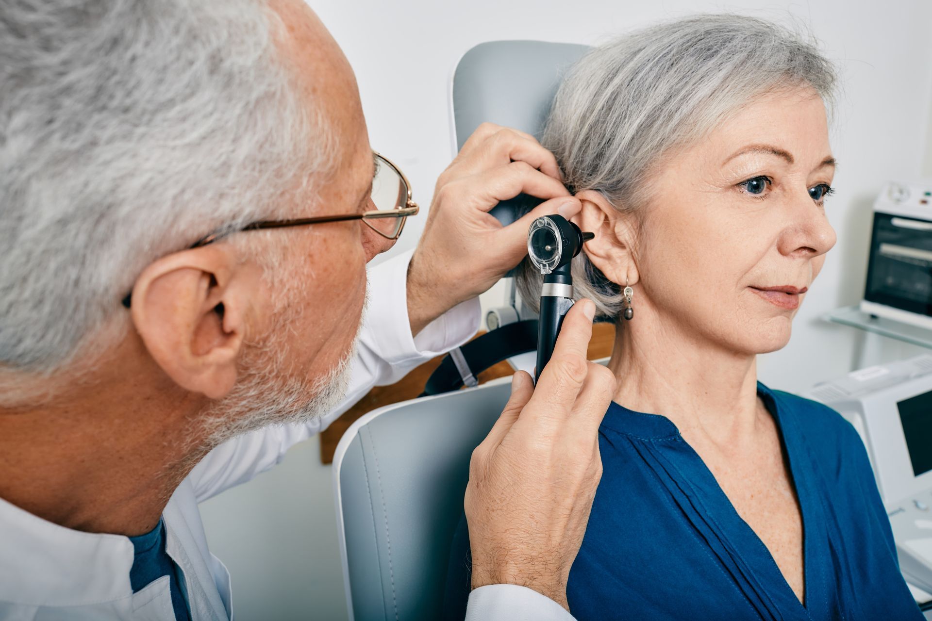Older man receiving an ear examination from an audiologist or doctor using an otoscope, highlighting