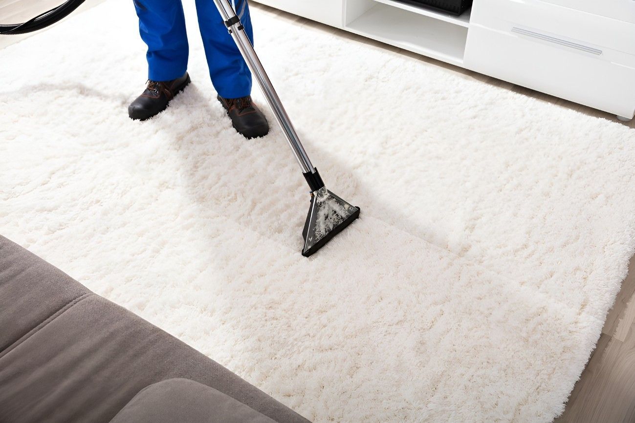 A Man is Vacuuming a White Rug in a Living Room — Kristal Kleen Services in Jubilee Pocket, QLD