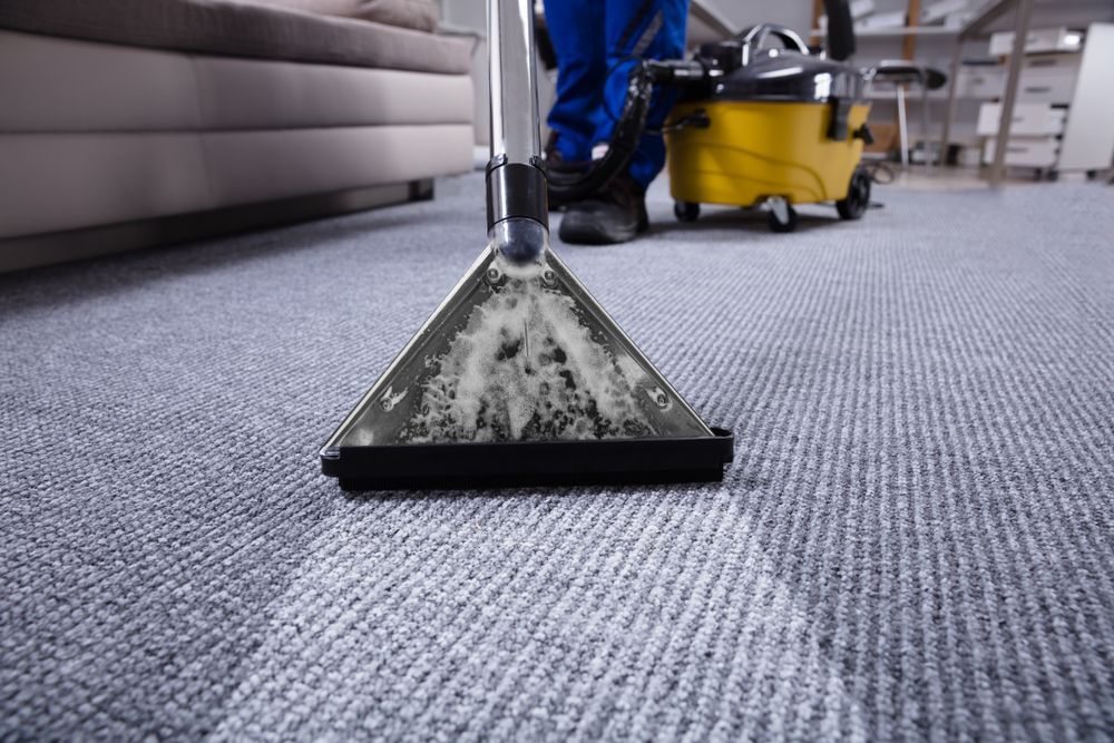 A Person Is Cleaning A Carpet With A Vacuum Cleaner — Kristal Kleen Services in Bowen, QLD