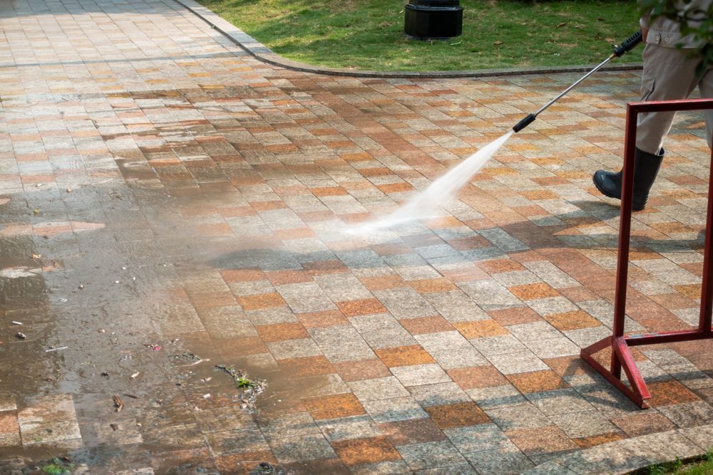 A Person Is Using A High Pressure Washer To Clean A Brick Driveway — Kristal Kleen Services in Jubilee Pocket, QLD