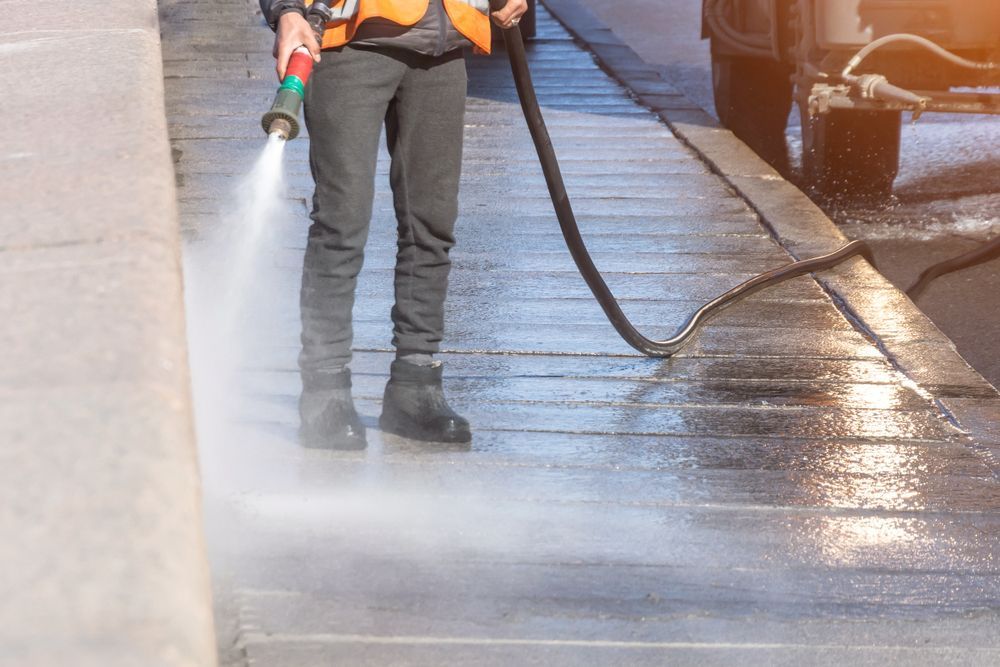 A Man Is Using A High Pressure Washer To Clean A Sidewalk — Kristal Kleen Services in Bowen, QLD