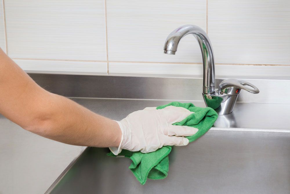 A Person Is Cleaning a Stainless Steel Sink with A Green Cloth — Kristal Kleen Services in Bowen, QLD