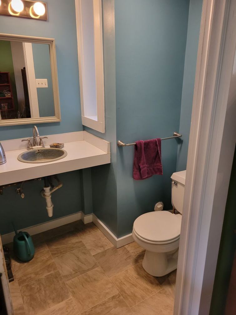 Small bathroom with teal walls, white vanity and toilet, and a pink towel on a chrome rack.