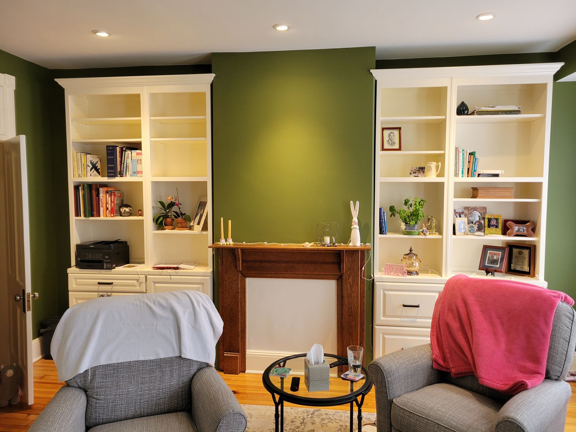 Cozy living room with green accent wall, white built-in shelves, fireplace, and two upholstered chairs.