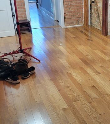 Shoes and a coat rack on a polished wooden hallway floor beside brick walls