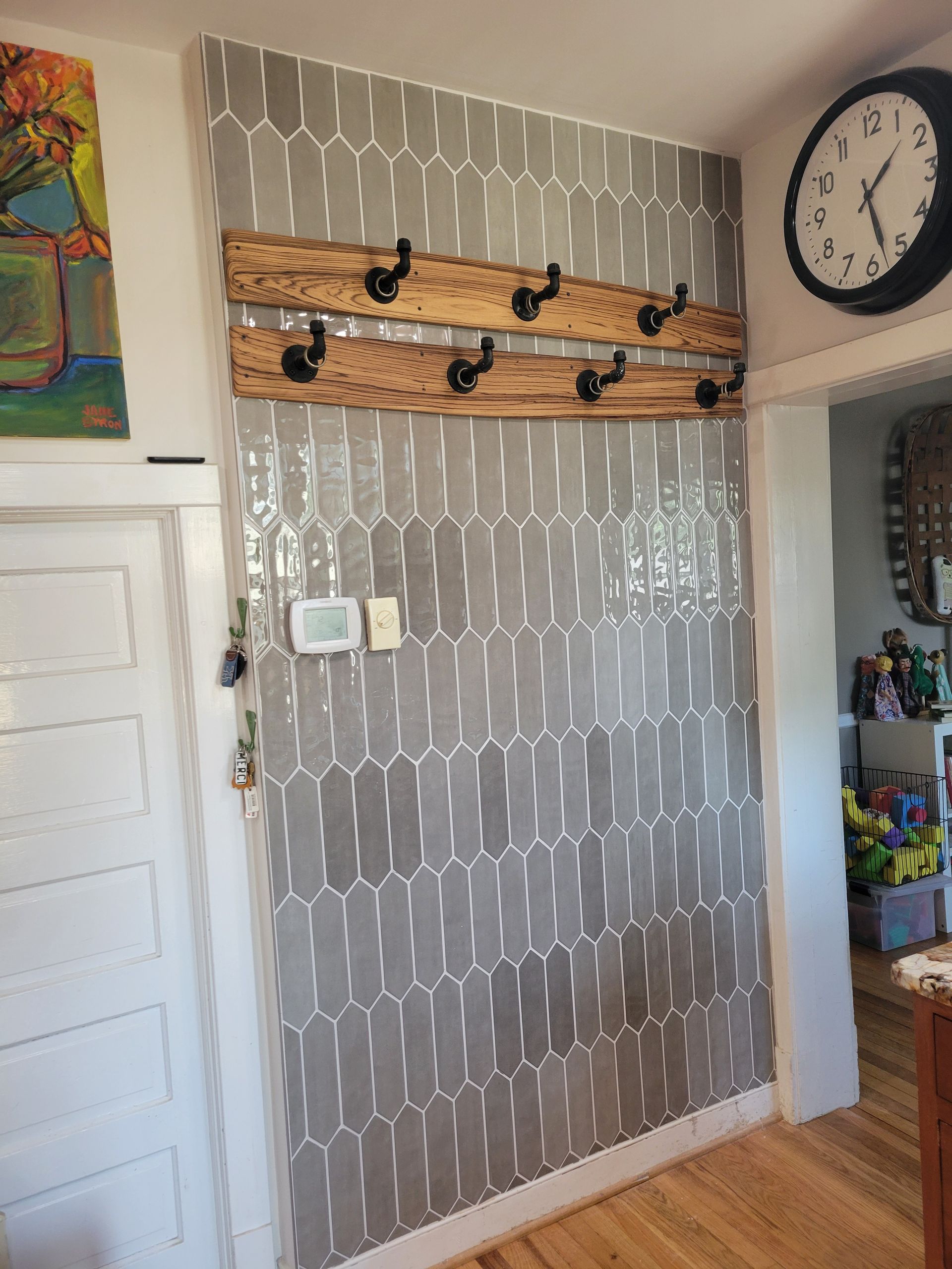 Hallway wall with patterned wallpaper, wooden coat rack, clock, and adjacent doorway to a kitchen area