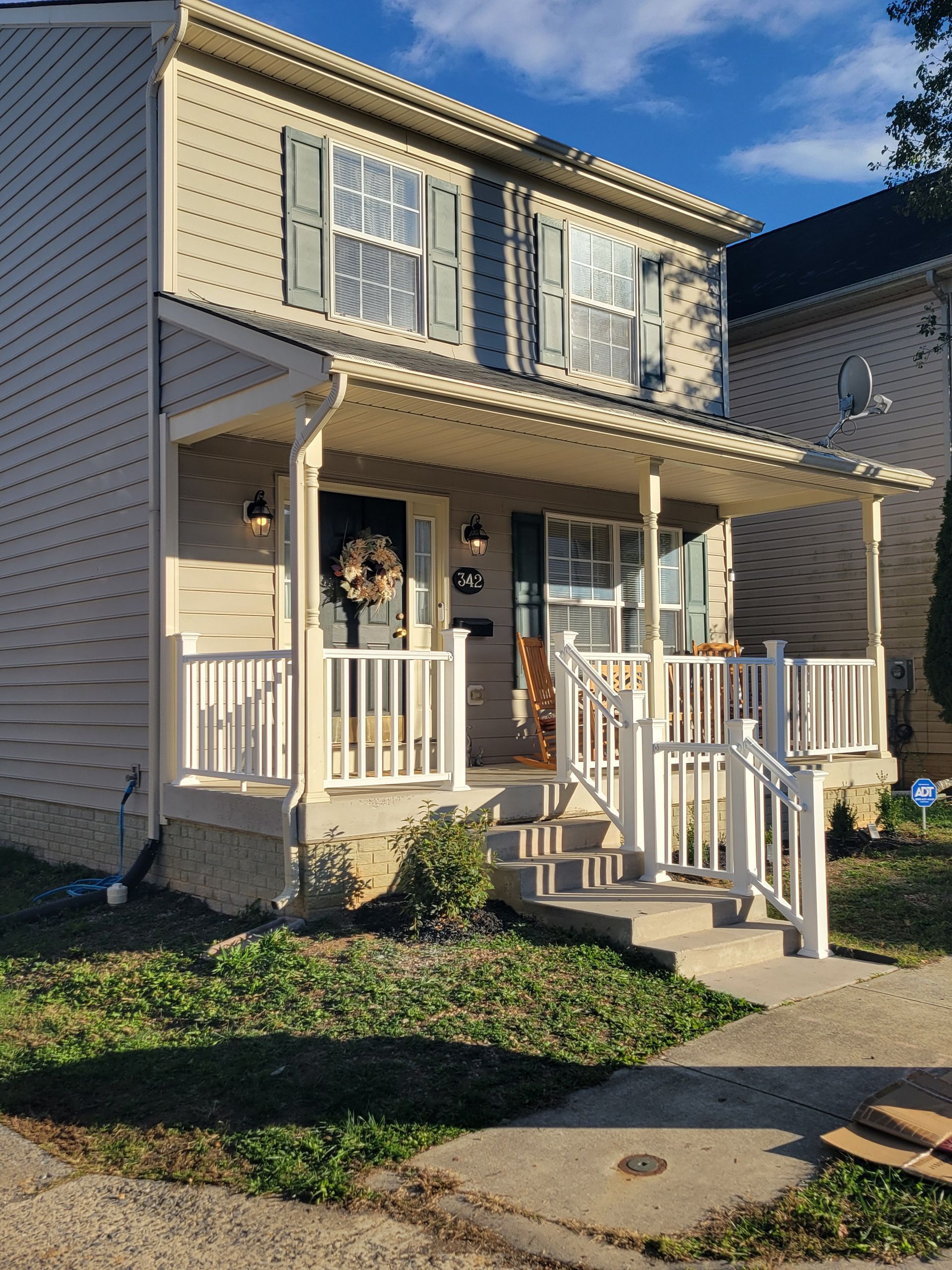 Two-story beige house with a small front porch, white railings, and steps leading to the entrance.