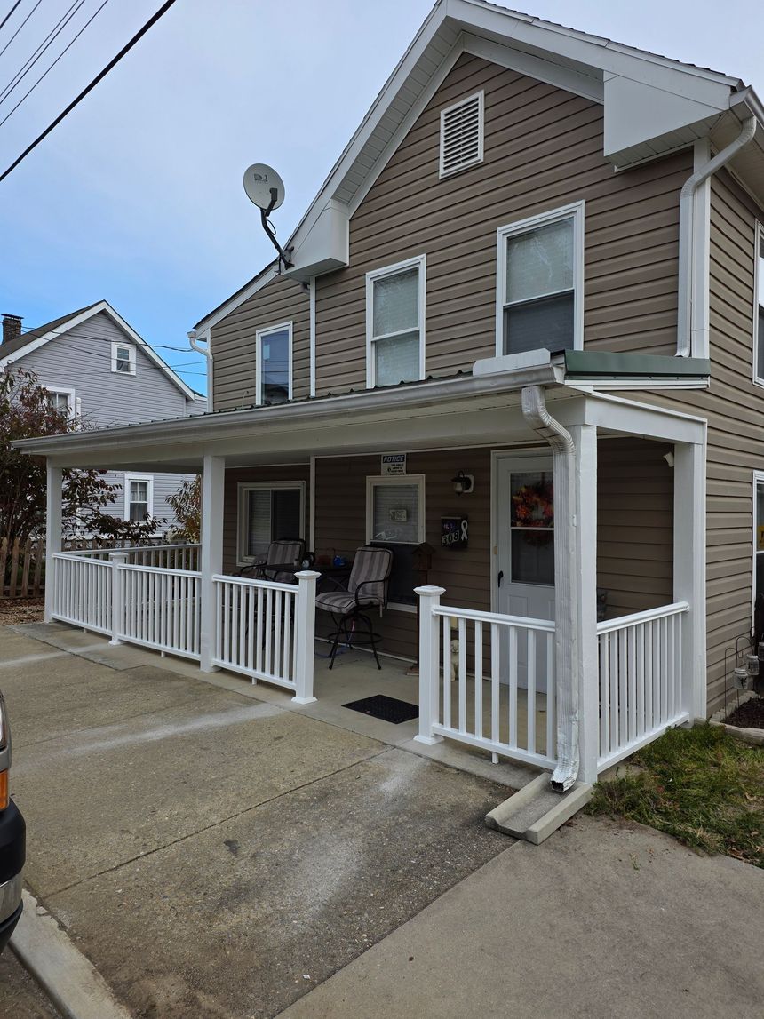 Two-story house with beige siding, white porch railings, and a covered front porch on a paved driveway
