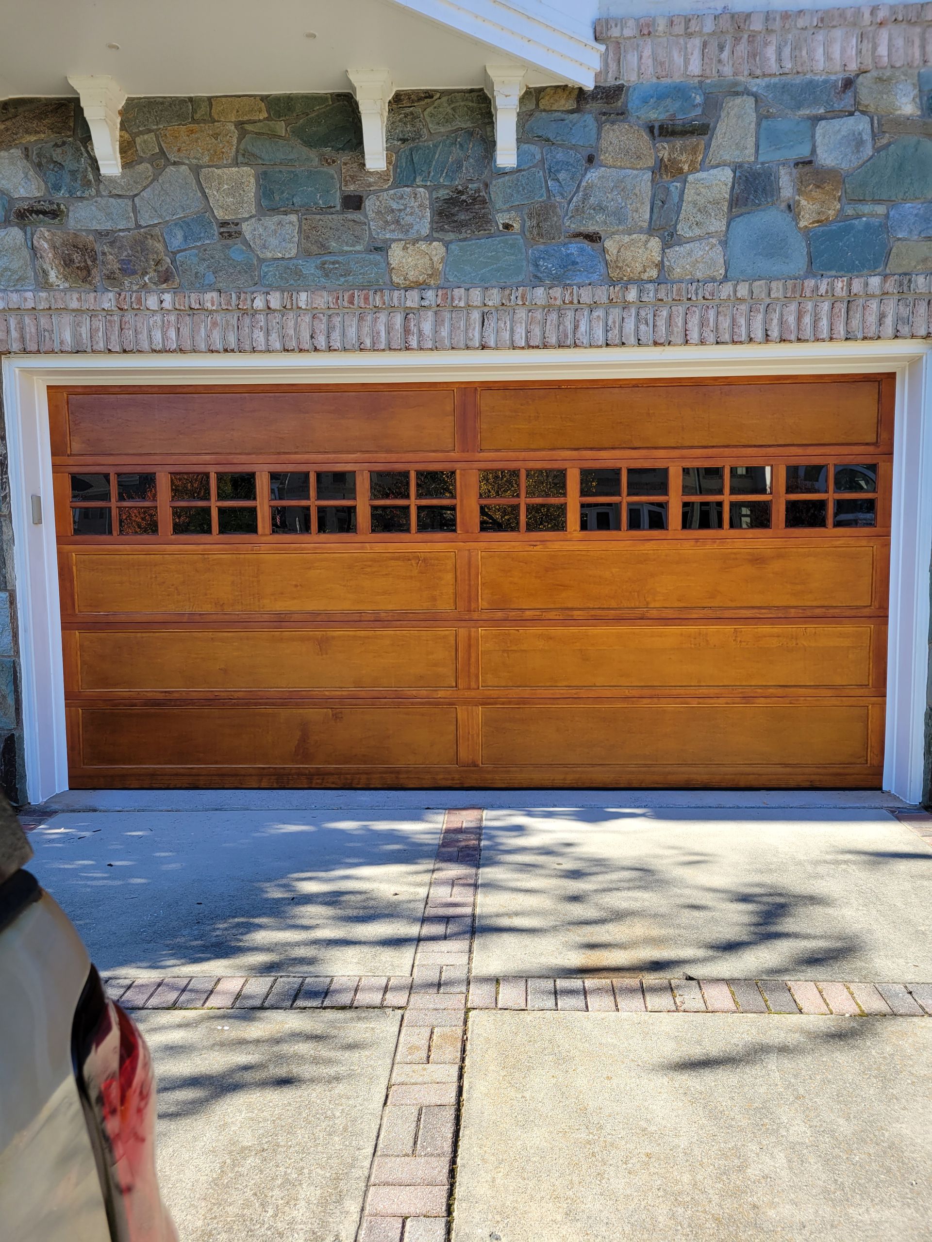 Wooden garage door with small windows set in a stone facade, viewed from a driveway