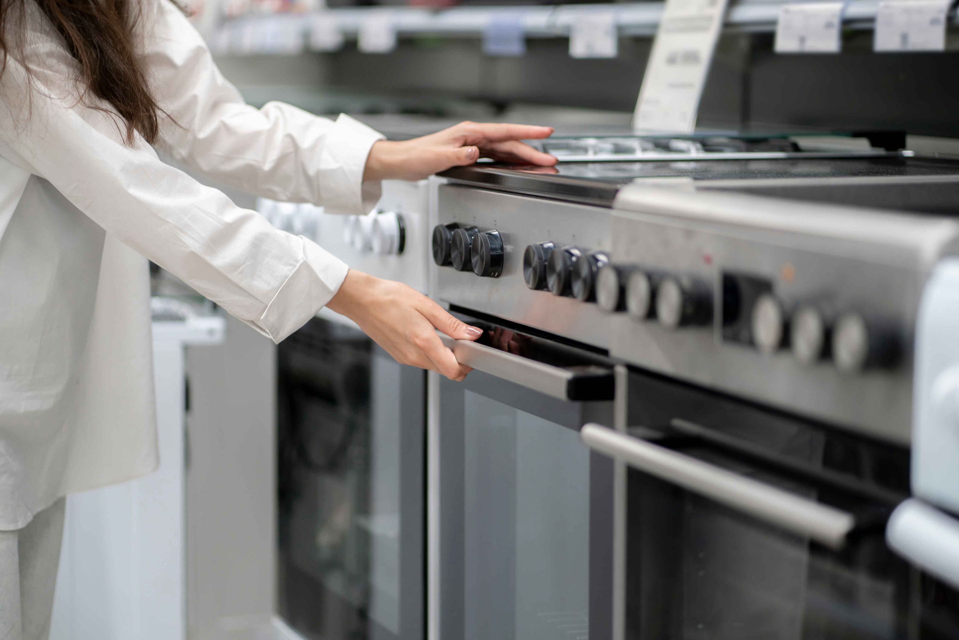 Une personne examine un four dans un magasin, ouvre la porte et touche la poignée.