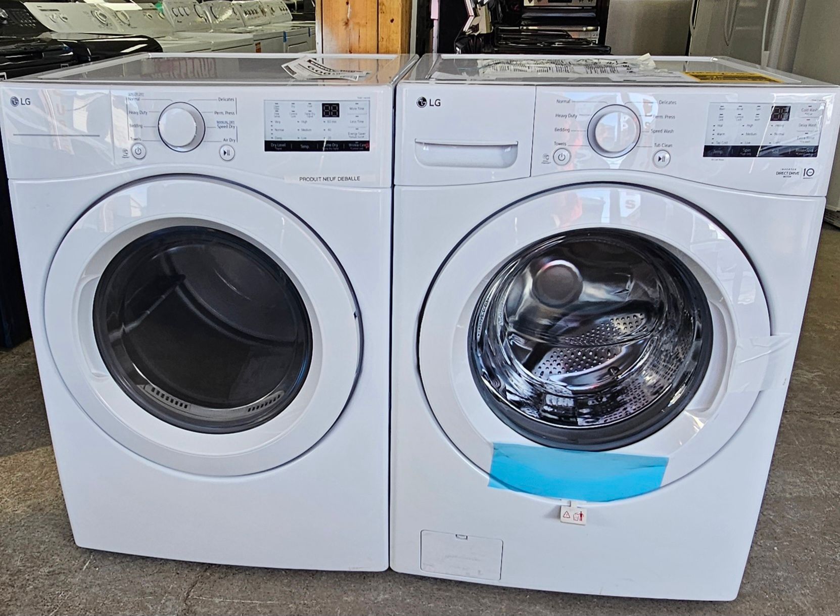 Deux machines à laver à chargement frontal, blanches, côte à côte dans une buanderie ; la porte de droite est recouverte de plastique.
