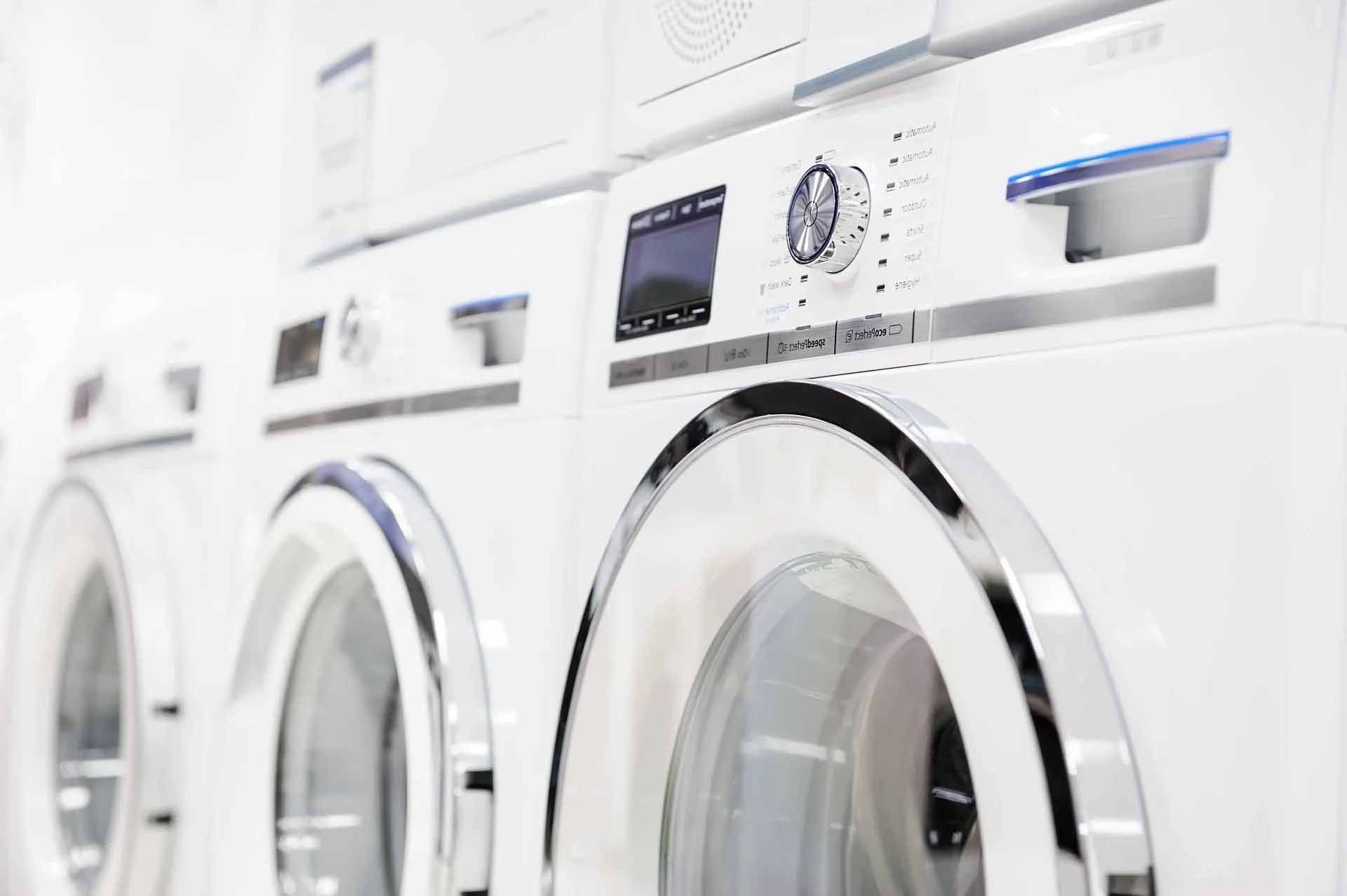 Rangée de machines à laver blanches aux accents chromés, dans un décor lumineux.