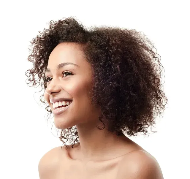 Woman with curly dark hair smiling, looking to the side. Bare shoulders, white background.