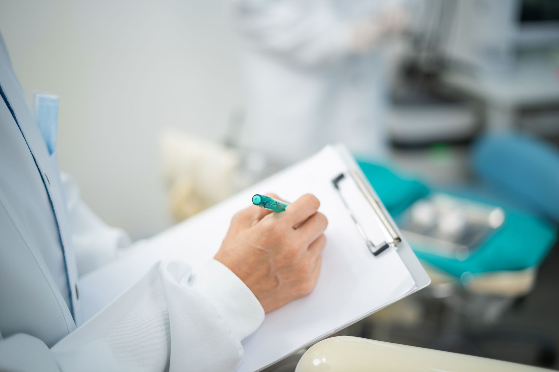 Doctor in white coat writing on clipboard in dental office.