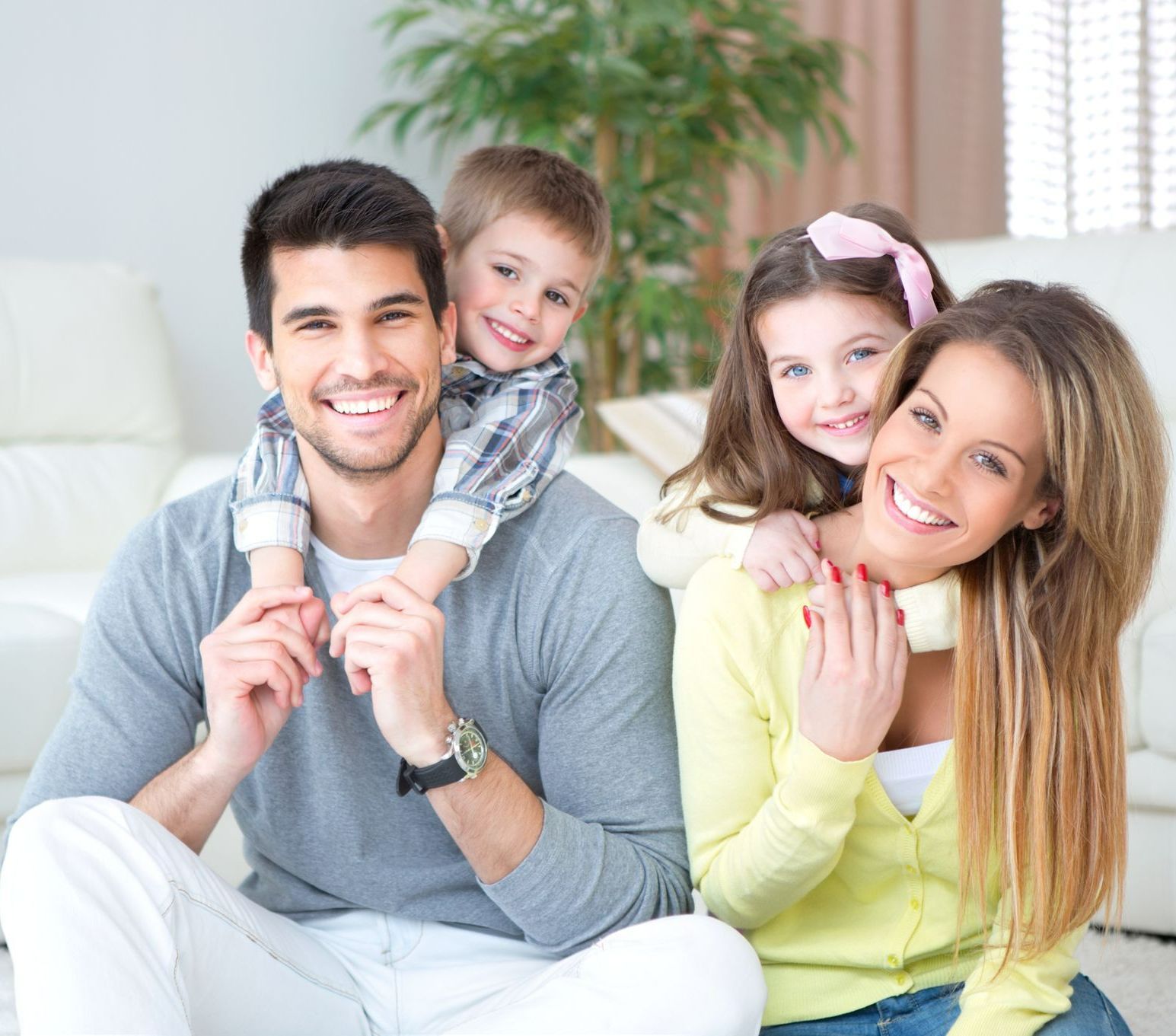 Family smiling, posing together indoors. Dad holding son, mom with daughter.