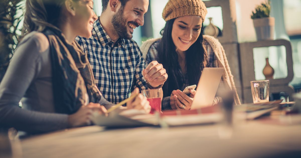People gathered around a table, smiling and working together with a laptop in a cozy indoor setting