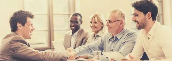 Business meeting with five people smiling and shaking hands around a conference table