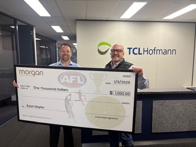 Two men holding a giant ceremonial check in an office lobby with TCLHoffmann signage.