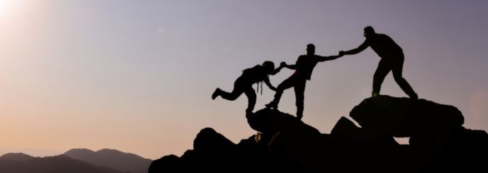Silhouetted hikers helping each other climb rocky peaks at sunset