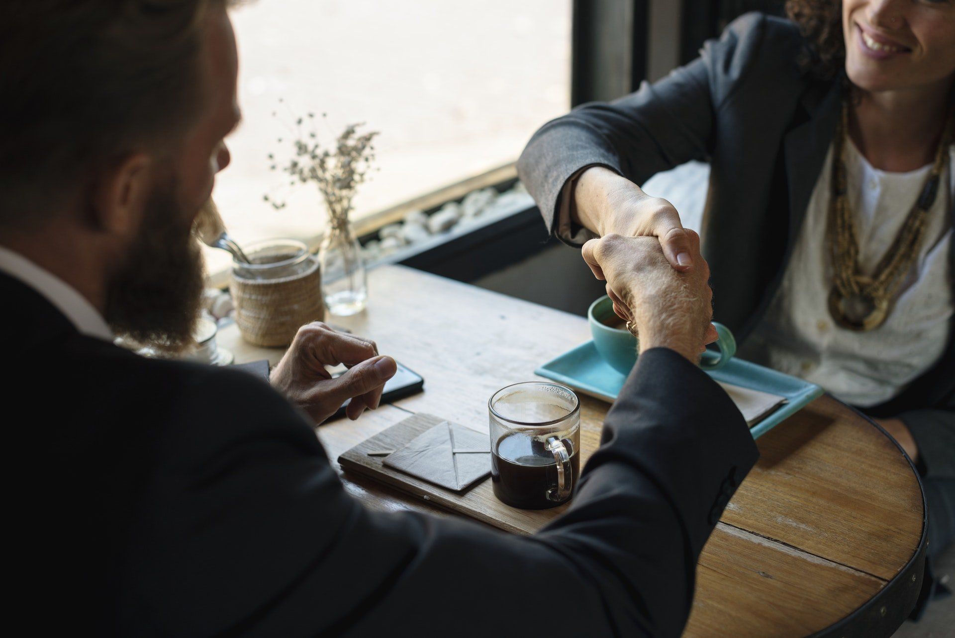 Two people shaking hands across a café table with coffee cups and a tablet