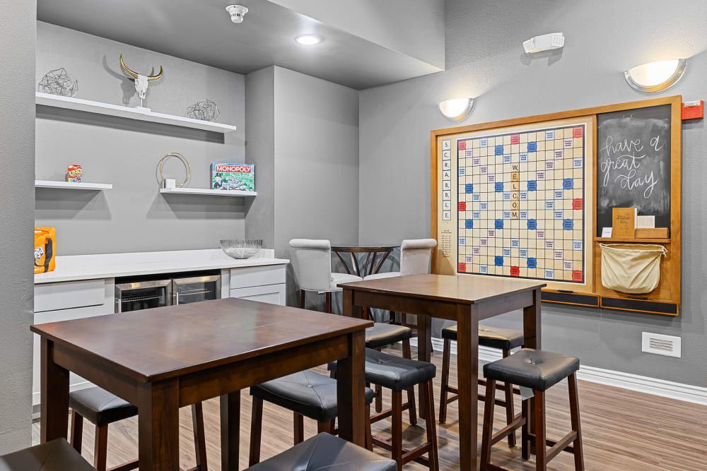Resident lounge with tables and chairs and a scrabble board on the wall at Marquis at Town Centre in Broomfield, CO.