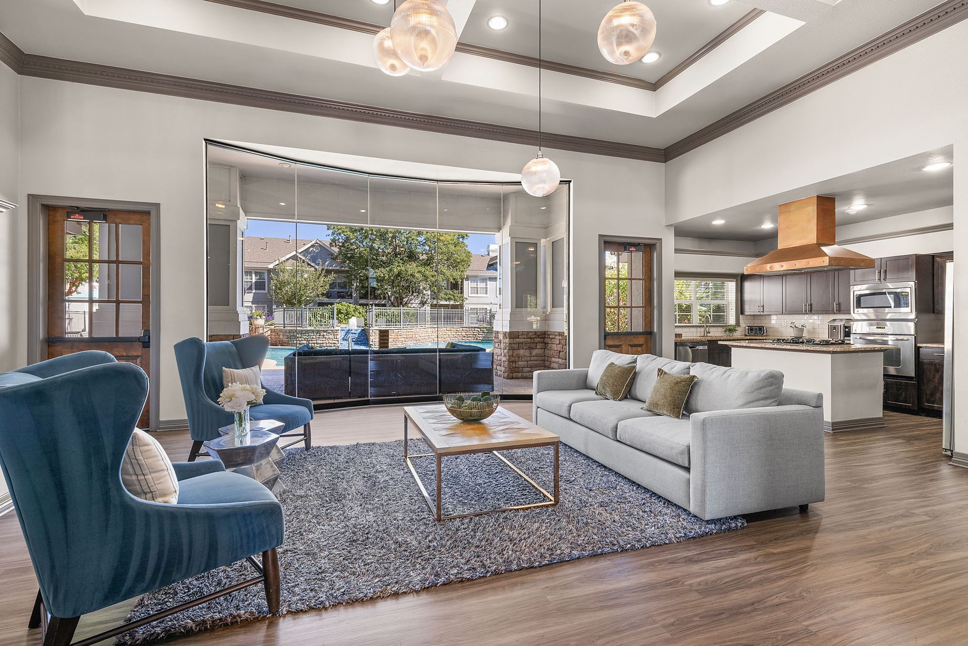 Bright open-plan living room with gray sofas, blue chairs, a coffee table, and a kitchen in the background at Marquis at Town Centre in Broomfield, CO.