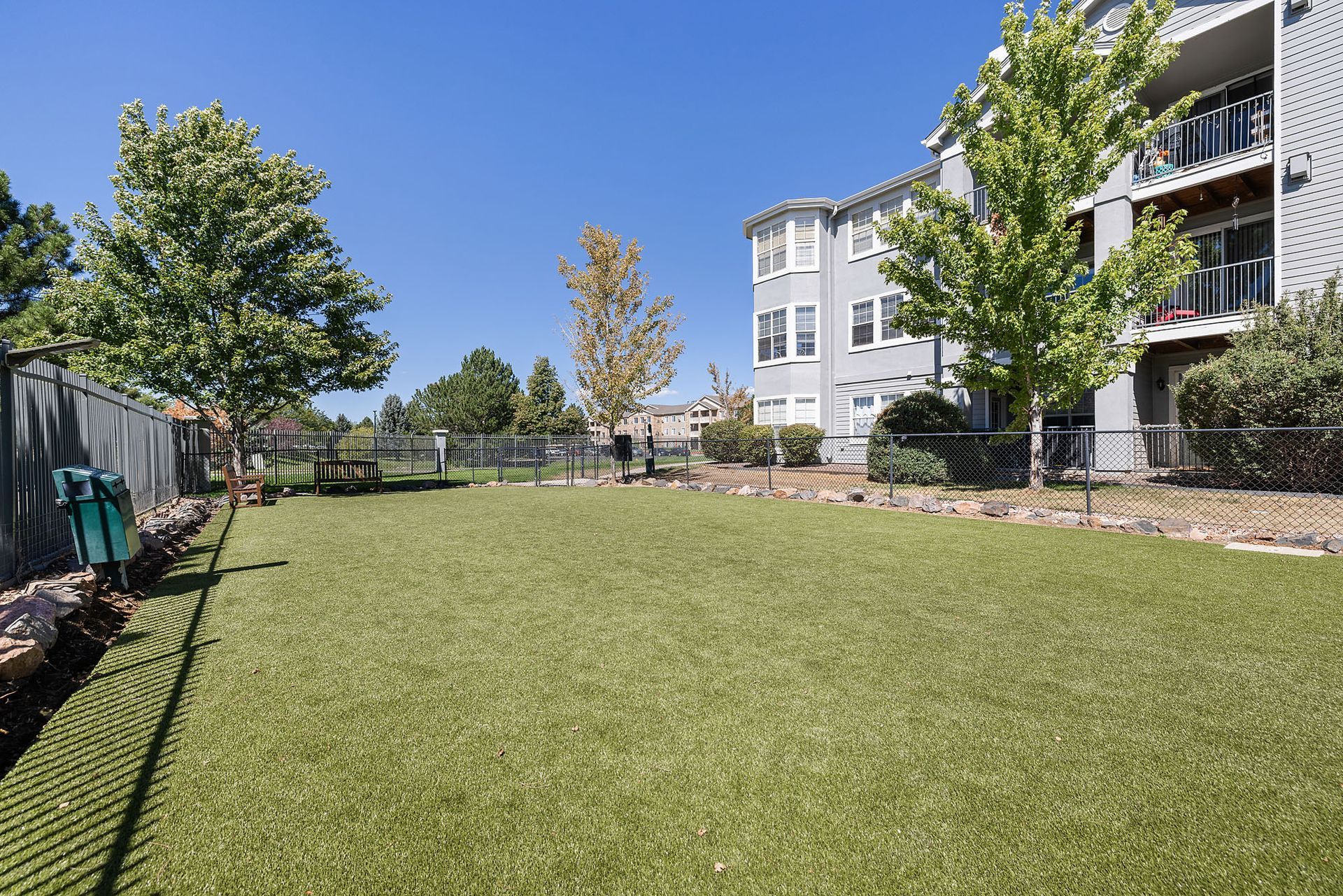 Apartment courtyard with a large grassy lawn, trees, and balconies under a clear blue sky at Marquis at Town Centre in Broomfield, CO