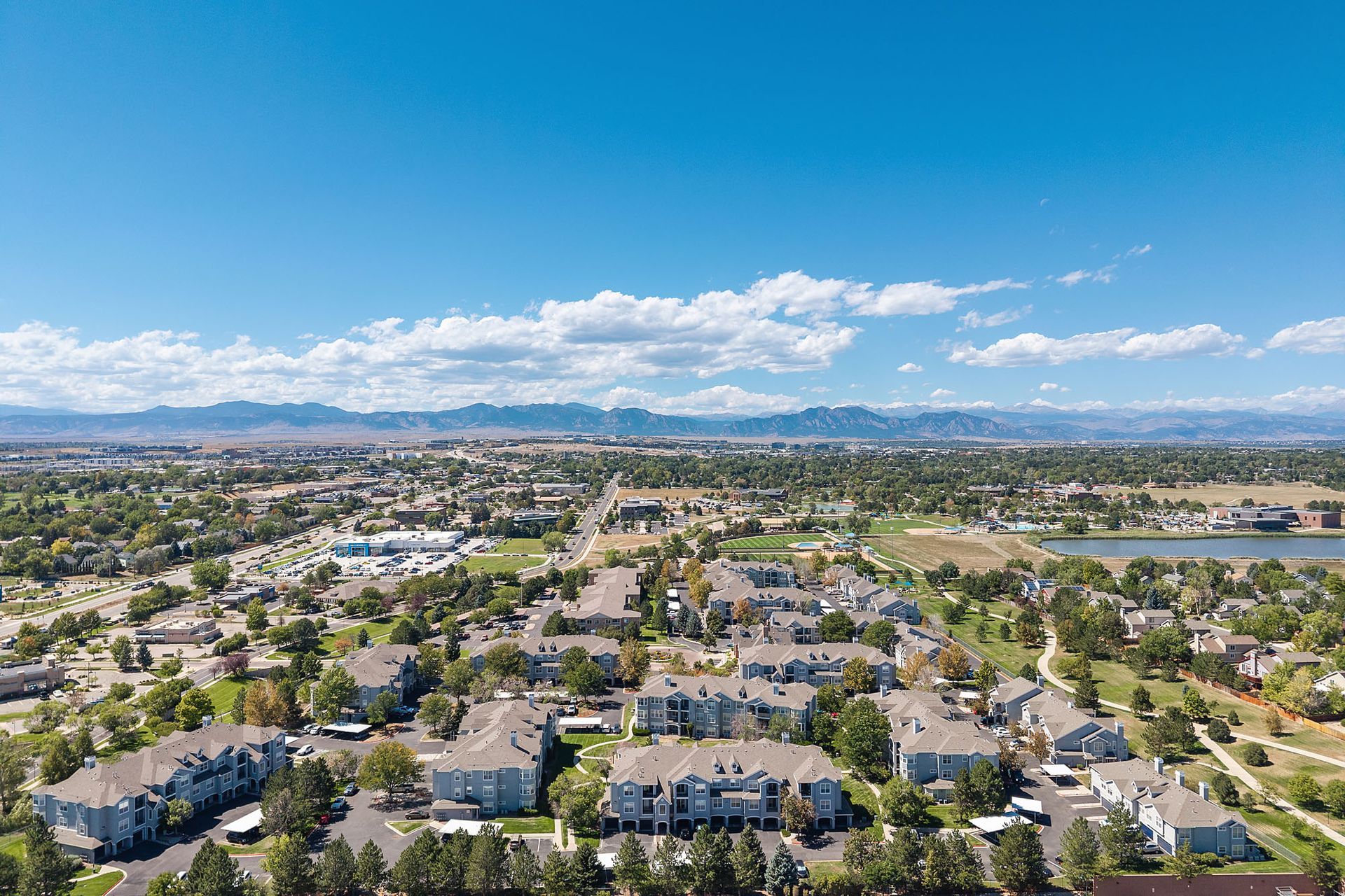 Aerial view of a suburban neighborhood with houses, streets, trees, and distant mountains under a blue sky at Marquis at Town Centre in Broomfield, CO.