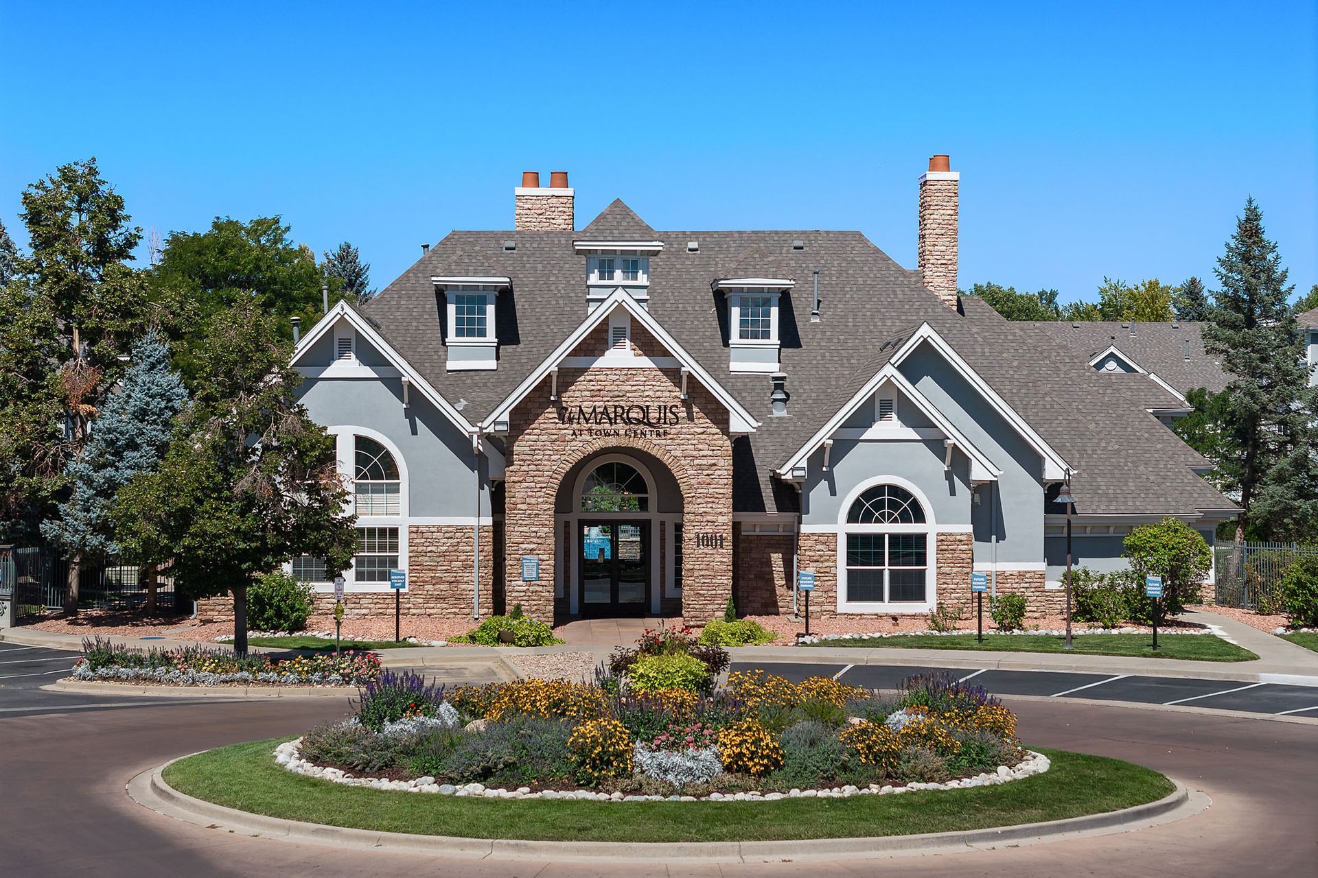 Stone suburban house with arched entry, flower bed, and circular driveway under a blue sky at Marquis at Town Centre in Broomfield, CO